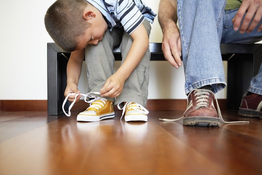 Мальчик учится завязывать свои шнурки на примере отцовской обуви 